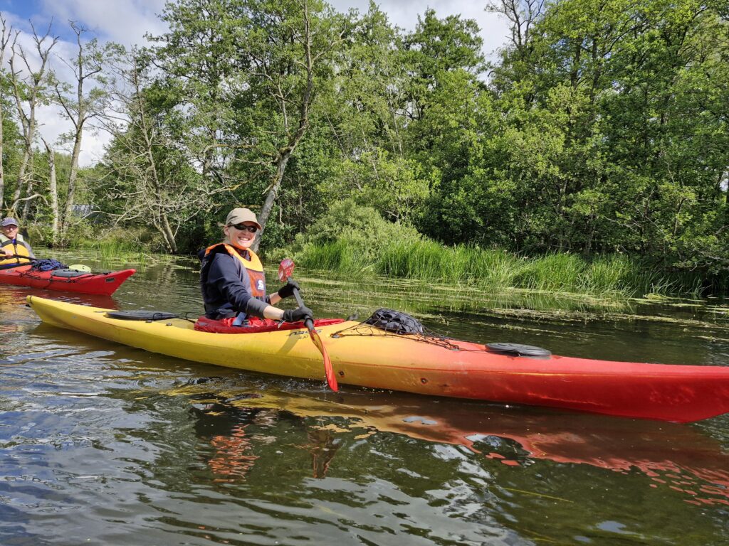 En kajak på Gudenåen med grønne træer i baggrunden