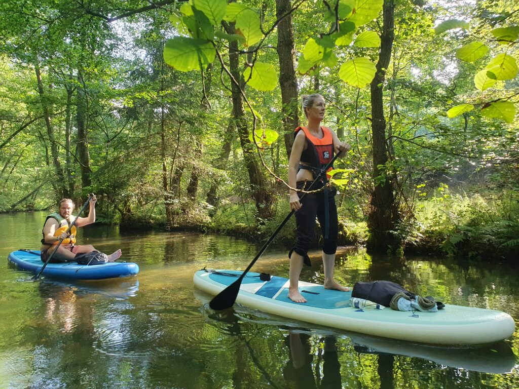To personer står på SUP på en lille å