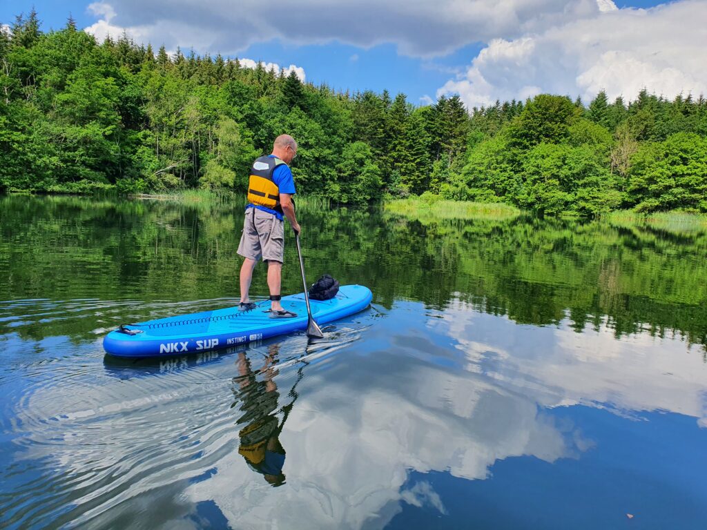 En mand på SUP med grønne træer som baggrund